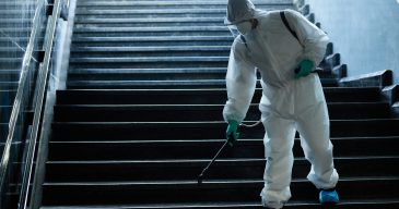 Man in protective suit disinfecting staircase of underground passage in order to prevent the spread of coronavirus.